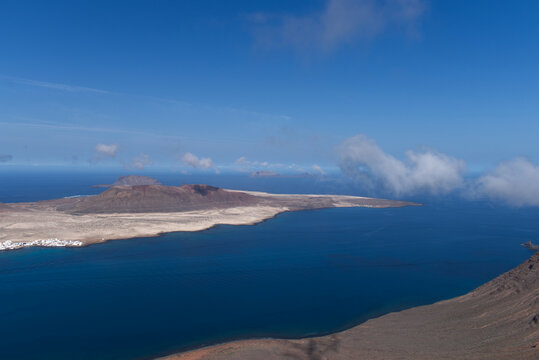 La Graciosa Island in the Canary Islands and a view of Montana Amarilla and the Parque Natural Archipielago Chinijo as clouds form in the channel between Lanzarote and La Graciosa.