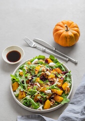 Salad with pumpkin, arugula, feta cheese, nuts and dried berries in a plate on a light background with soy or balsamic sauce.