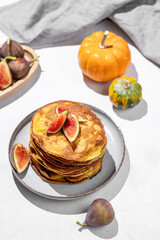 Stack of pumpkin pancakes with honey and figs on light background with fresh fruits and vegetables.