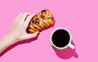 Hand holding a maple pecan bun on a pink background with cup of espresso coffee and shadow.