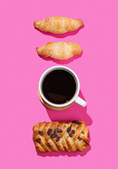 Flat lay of espresso coffee cup, fresh croissants and maple pecan bun on pink background with shadow.