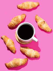 Flat lay of espresso coffee cup and fresh croissants on pink  background with shadow.