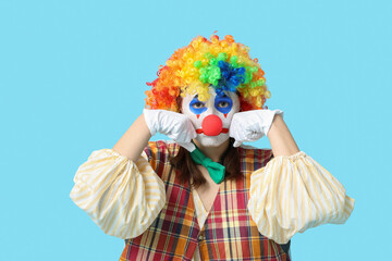 Young woman dressed as sad clown crying on blue background. April Fool's day celebration