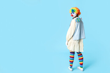 Young woman dressed as sad clown with paper fish attached to her back on blue background. April...
