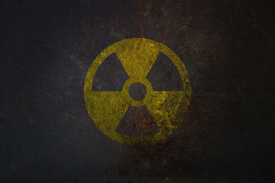 Radioactive (ionizing radiation) round yellow and black danger symbol painted on a massive rusty metal wall with dark rustic grunge texture background. Nuclear, radioactive alert concept.
