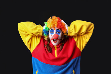 Young shocked woman dressed as sad clown on black background. April Fool's day celebration