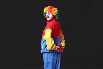 Young woman dressed as sad clown with whoopee cushion on black background. April Fool's day celebration