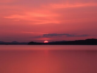 Obraz premium Soft pink and purple sunset over a calm lake, reflecting the silhouettes of distant mountains and trees, serene, sunset, sky