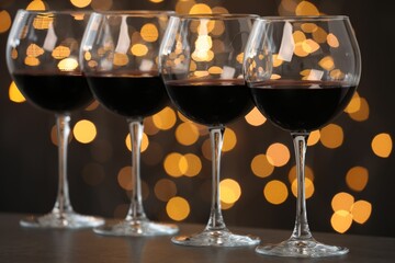 Tasty red wine in glasses on table against dark background with blurred lights, bokeh effect