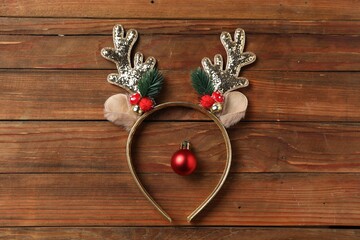 Beautiful reindeer headband and Christmas bauble on wooden background, top view