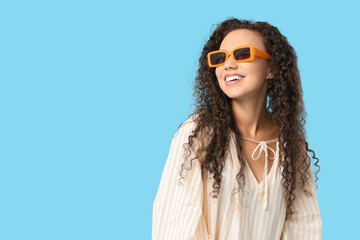 Beautiful African-American woman with sunglasses on blue background