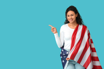 Beautiful young happy African-American woman with USA flag pointing at something on blue background