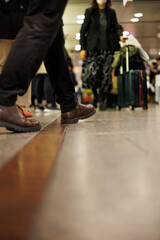 Busy people in busy places - a close-up low angle view of a businessman in casual dress walking towards a woman pushing a dark green suitcase in a crowded indoor area  depicts daily active life.