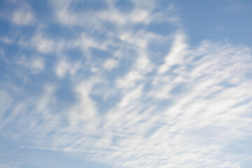 Hazy cirrus clouds form a grid like pattern in the light blue of the daytime sky. The interweaving pattern of soft white with intermittent spots of light blue creates a serene symmetrical cloudscape.