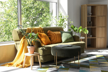 Comfortable sofa, pouf and plants near large window in living room