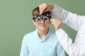 Female ophthalmologist customizing optical trial frame for little boy on green background