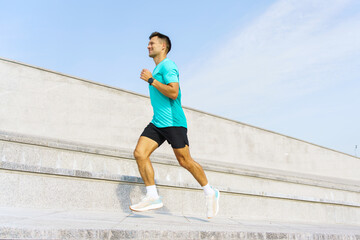 Man running up outdoor steps in a turquoise shirt under a clear blue sky during daylight