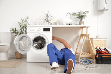 Mature male plumber installing washing machine in bathroom