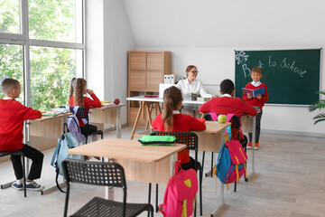 Little pupils with teacher having lesson in classroom