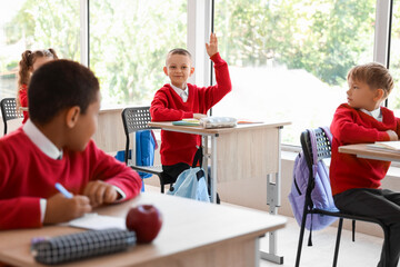 Little schoolboy raising hand during lesson in classroom