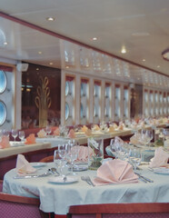Formal and elegant ocean view dining room restaurant onboard historic luxury cruiseship or cruise ship liner with set tables in classic  interior design style and ceiling ambient lighting