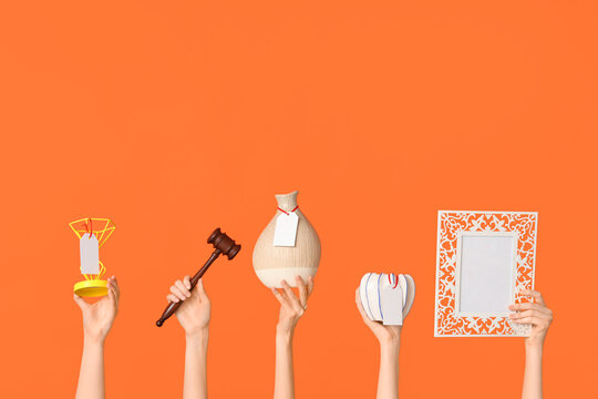 Female hands with auction gavel and antique items on orange background