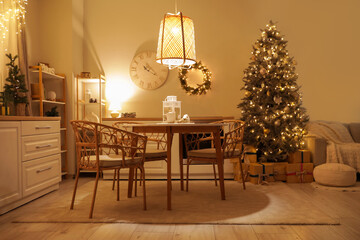 Interior of dark kitchen with glowing Christmas tree, dining table and counters at night