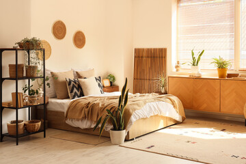 Interior of cozy bedroom with plants, shelf unit and commode