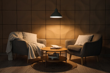Interior of dark living room with armchairs, table and glowing lamp at night