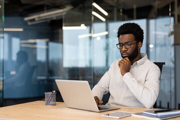 African American businessman thinking laptop work. Capturing thoughtful expression, business attire, office ambiance. Represents focus, technology usage, corporate environment, decision making.