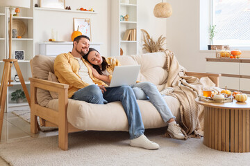 Happy young couple with laptop sitting at home on autumn day