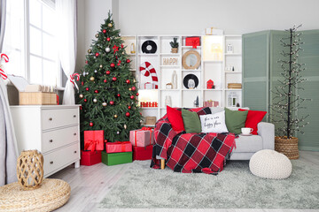 Interior of living room decorated for Christmas with sofa, shelving unit and dresser near window