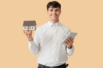 Male real estate agent with house model and tablet computer on beige background