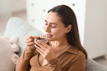 Beautiful young woman with glass cup of hot cocoa sitting on sofa in living room