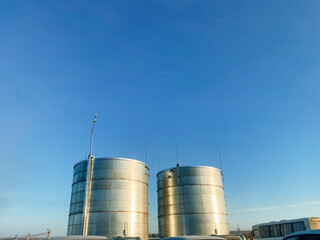 Two large, shiny stainless steel tanks stand tall against a vibrant blue sky, providing essential storage for various liquids, including gas, within an urban engineering landscape