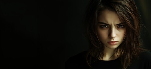 Naklejka premium Intense expression of young woman, dark background, serious gaze, long hair, natural makeup, emotional depth, portrait photography, copy space for text