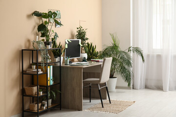 Stylish workplace with computer, notebooks and different houseplants near beige wall at home