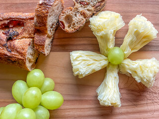 Cheese rosette. platter arrangement with grapes and rustic baguette bread slices on wood board, flat lay, top down, close up