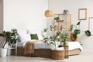 Interior of cozy bedroom with big bed, shelving unit and many different houseplants