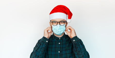 Portrait of young man in Santa hat wearing medical mask on white background.