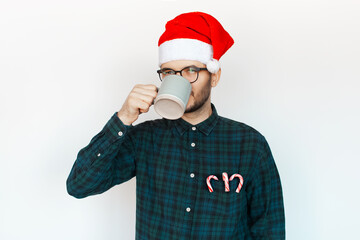 Portrait of young man in Santa hat drinking cacao on white background.