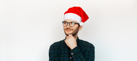 Portrait of young thoughtful man who looking away, wear Santa hat and glasses on white background.