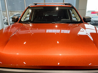 This image features a detailed closeup of an eyecatching orange car displayed within a modern showroom setting, showcasing its sleek design and vibrant color, drawing attention