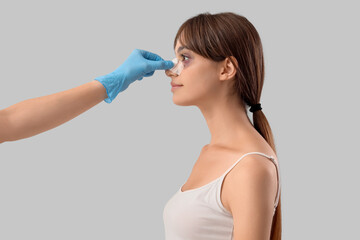 Surgeon hand touching woman's bandaged nose after plastic surgery on grey background