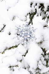 Silver crystal snowflake ornament hanging on a snowy tree branch. Winter background.