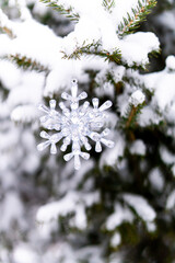 Silver crystal snowflake ornament hanging on a snowy tree branch. Winter background.