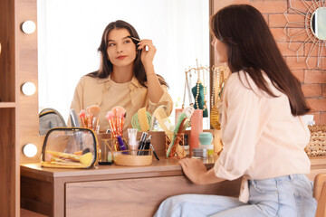 Beautiful young woman brushing her eyebrows near mirror at home