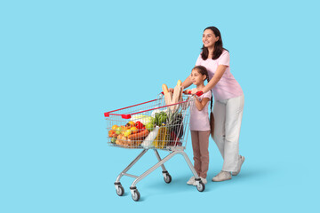 Beautiful young happy mother and her daughter with full shopping cart on blue background © Pixel-Shot