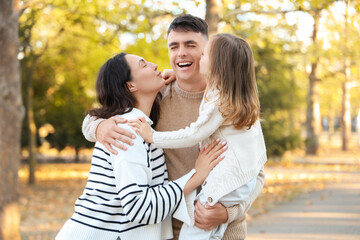 Fototapeta premium Happy mother and her daughter kissing father in beautiful autumn park
