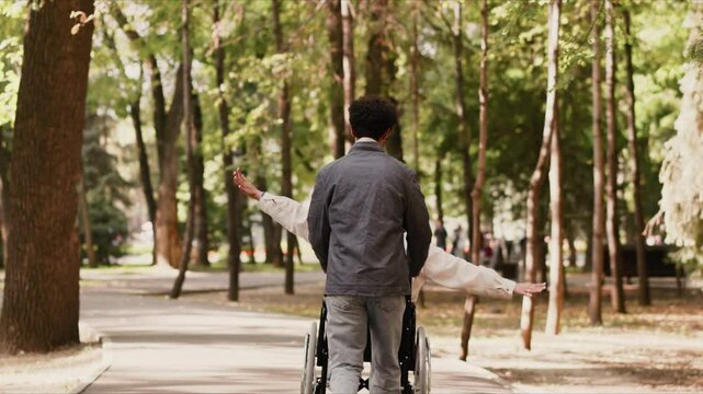 Young man pushing disabled girlfriend in wheelchair in park
